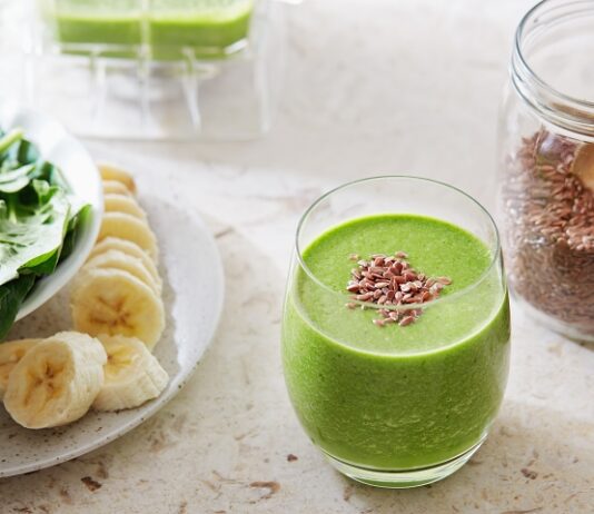 Easy Flax Seed Smoothie Overhead shot of green flax seed smoothie in a drinking glass with brown flax seeds sprinkled on top