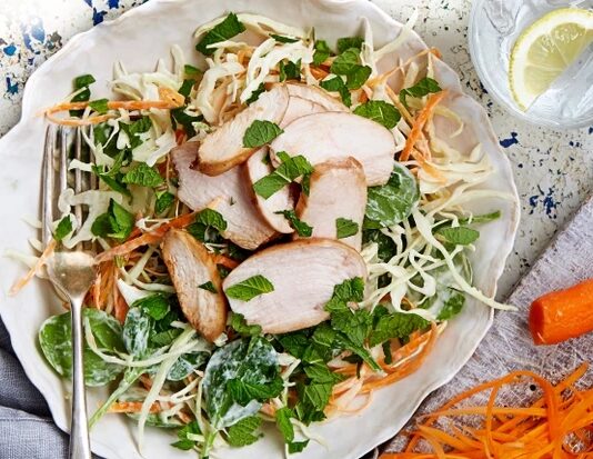 Mint Salad With Pomegranate Chicken Salad in white dish with pieces of chicken, cheese and lots of mint leaves