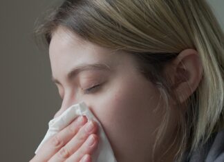 Common Cold Young woman with cold holds a tissue to her nose