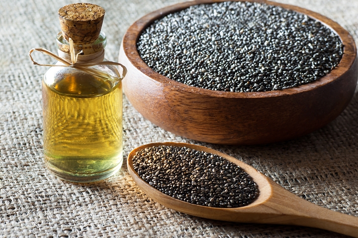 Decanter of chia oil next to a wooden bowl full of dark chia seeds