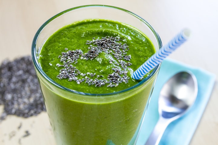 Chia seeds on surface of a green-colored smoothie in tall glass